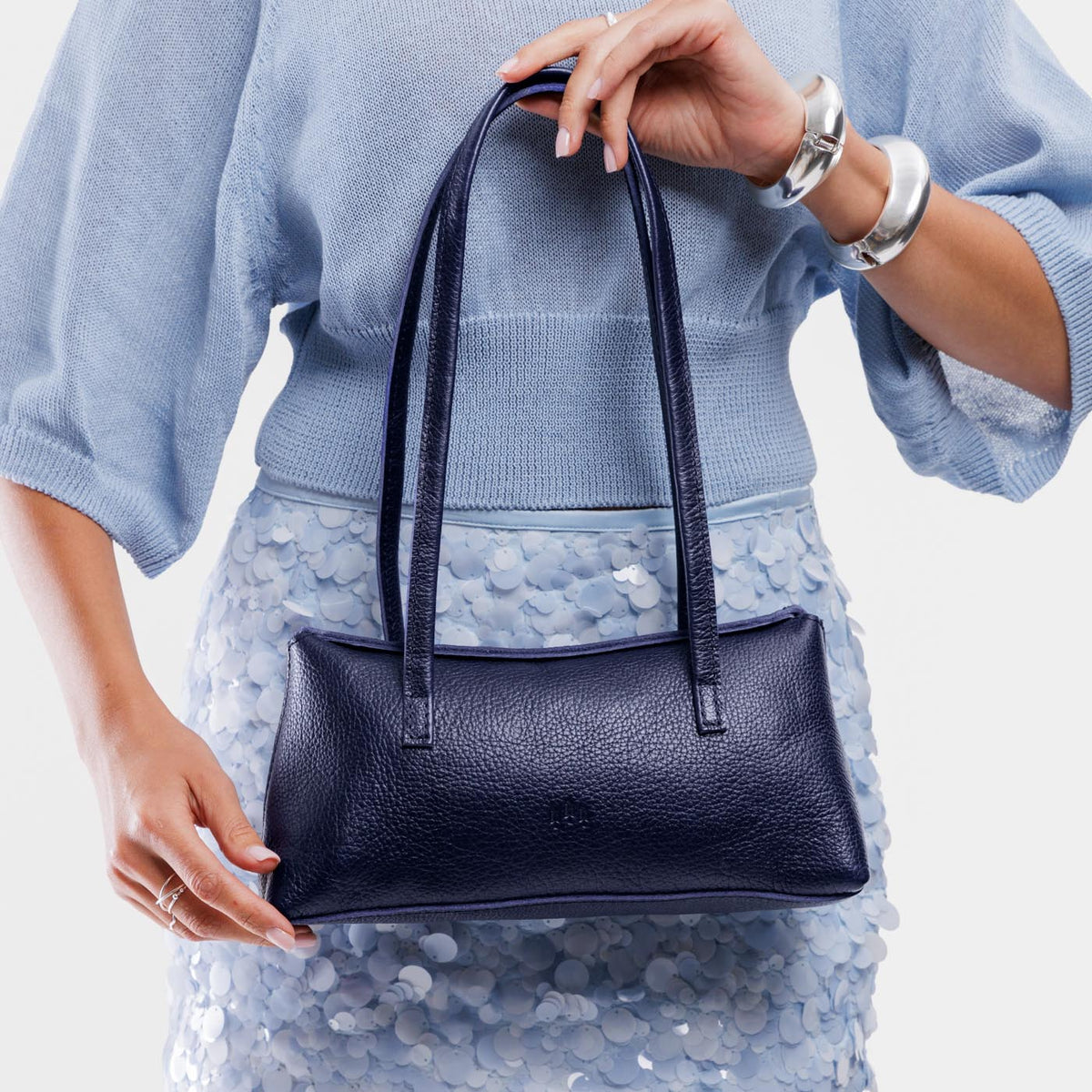 Cobalt | Woman holding a dark blue leather bowler bag against a white background