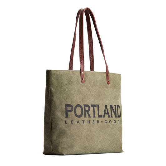 Green canvas tote bag with 'Portland Leather Goods' text and leather handles