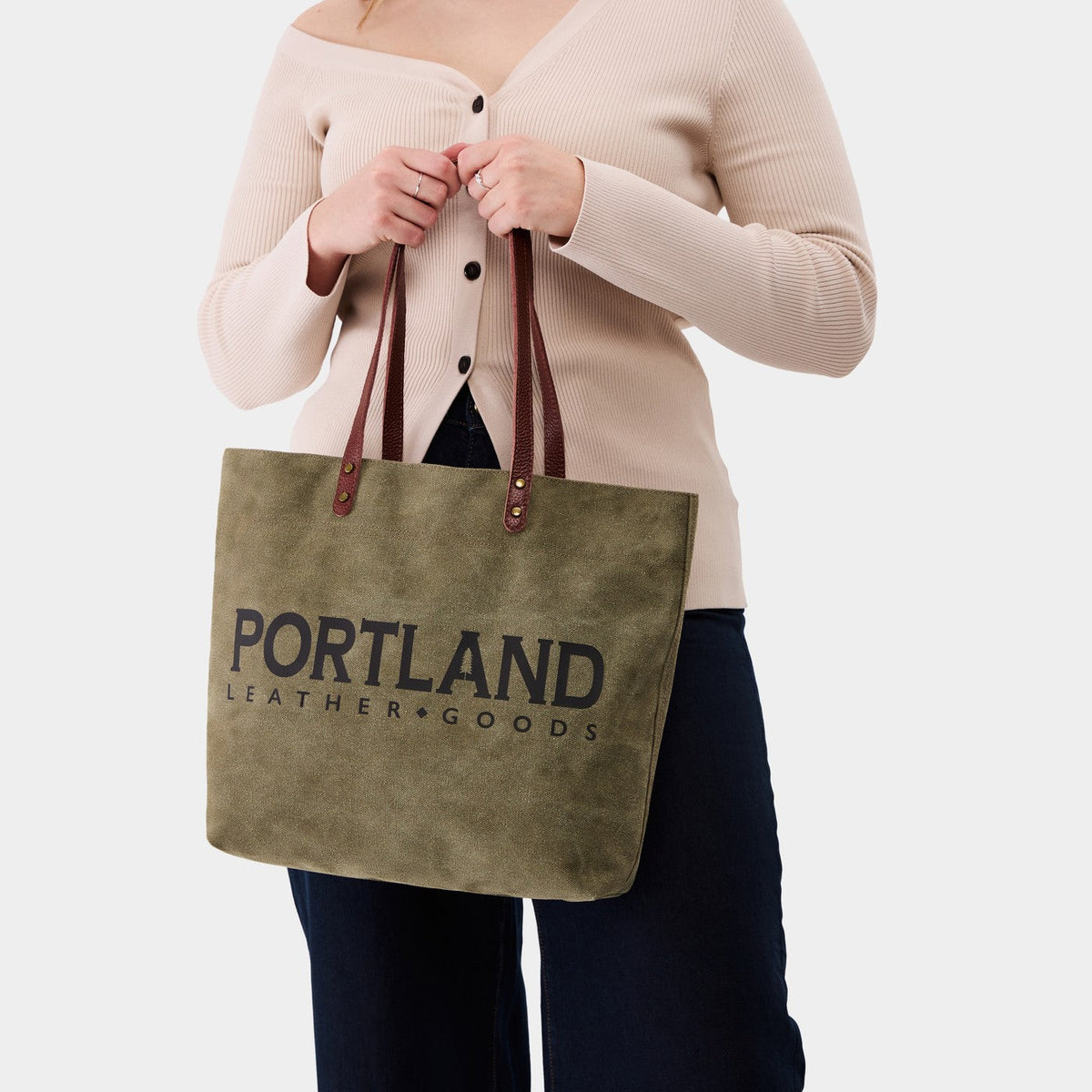 Person holding a green canvas tote bag with 'Portland Leather Goods' branding.