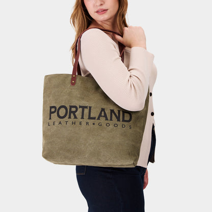 Person holding a green canvas tote bag with 'Portland Leather Goods' branding.