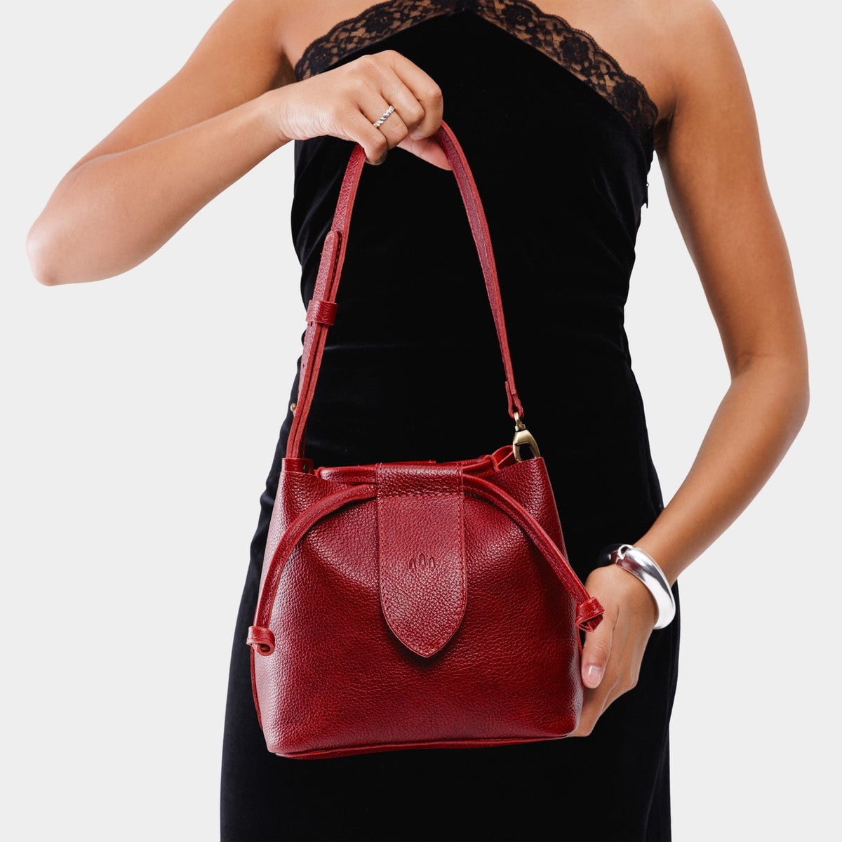 Chili Red*Small | Model holding symmetrical leather bag with leather drawstring closure and adjustable shoulder strap