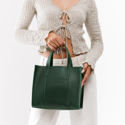 Aruba | Model holding structured mid-size tote bag with overlapping panels and crossbody strap