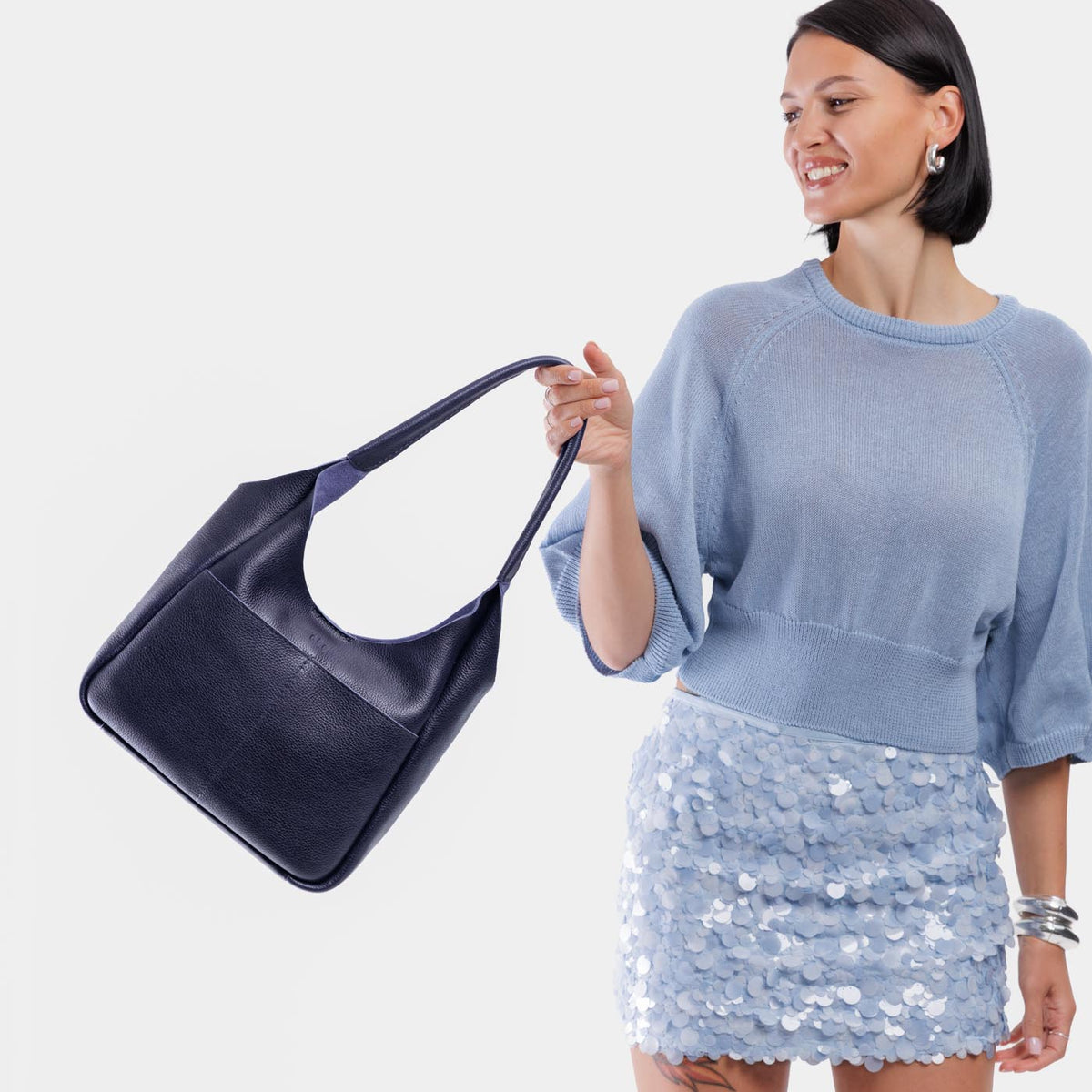 Cobalt*Large | A model holding a u-shaped, flat-bottomed leather shoulder bag with two outside pockets
