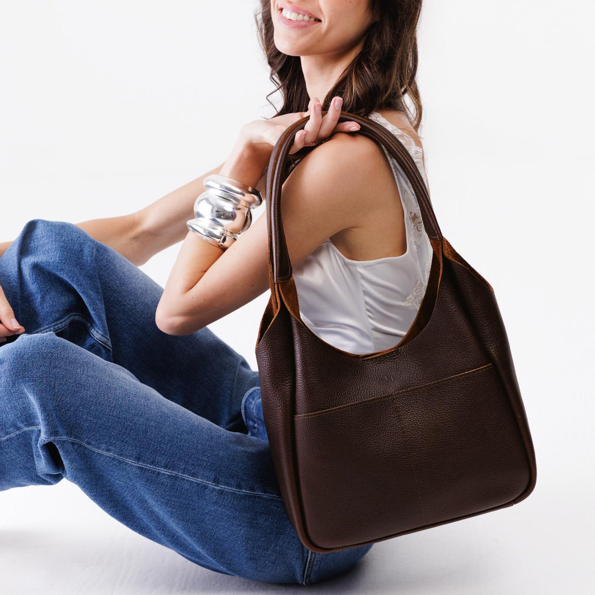 Coldbrew*Large | A model holding a u-shaped, flat-bottomed leather shoulder bag with two outside pockets