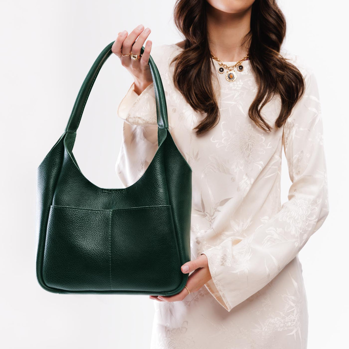 Forest Green*Large | A model holding a u-shaped, flat-bottomed leather shoulder bag with two outside pockets