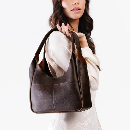 Coldbrew*Medium | A model holding a u-shaped, flat-bottomed leather shoulder bag with two outside pockets