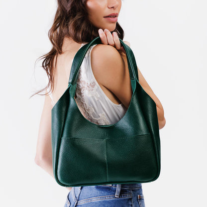 Forest Green*Medium | A model holding a u-shaped, flat-bottomed leather shoulder bag with two outside pockets