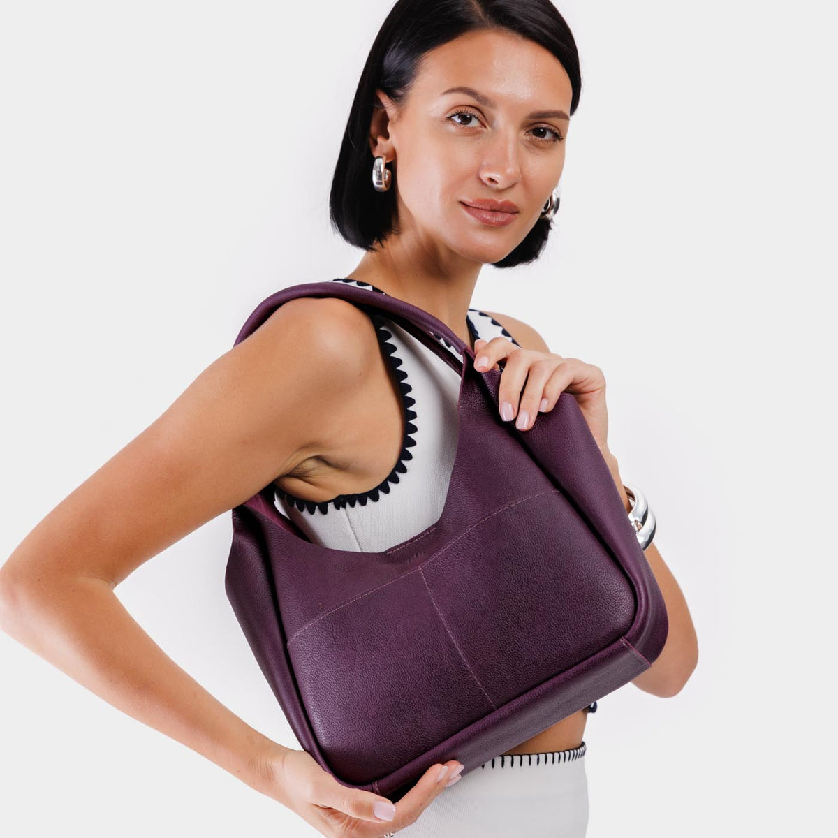 Plum*Medium | A model holding a u-shaped, flat-bottomed leather shoulder bag with two outside pockets