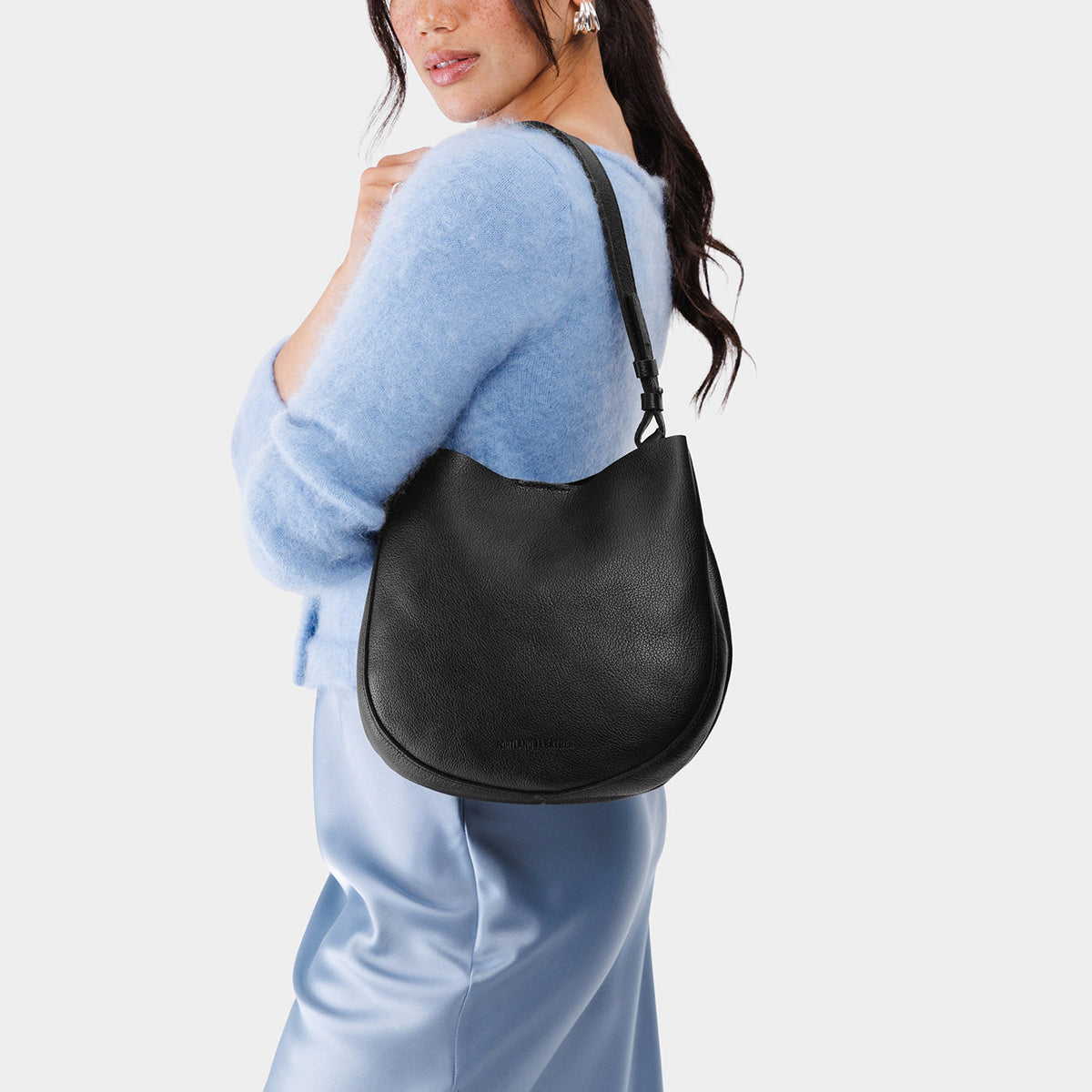 Pebbled--black*Medium | Woman wearing rounded shoulder bag with adjustable strap on a white background