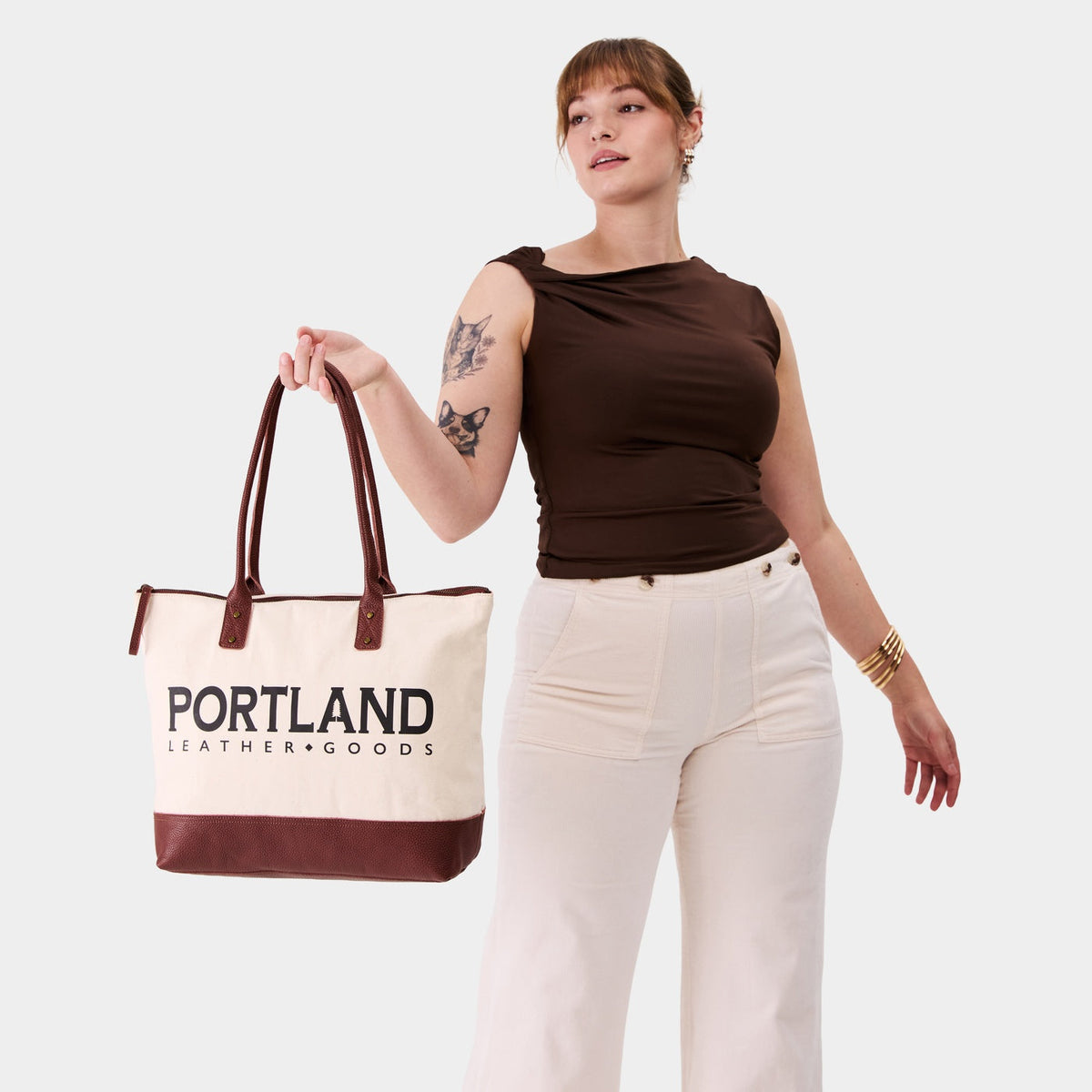 Model holding canvas tote with zipper, leather bottom, and leather handles on a white background